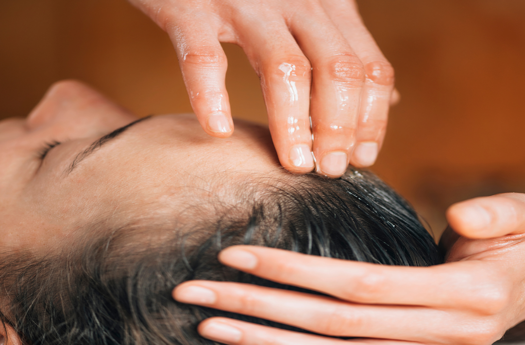 Hands massaging oil into the scalp during a hair treatment