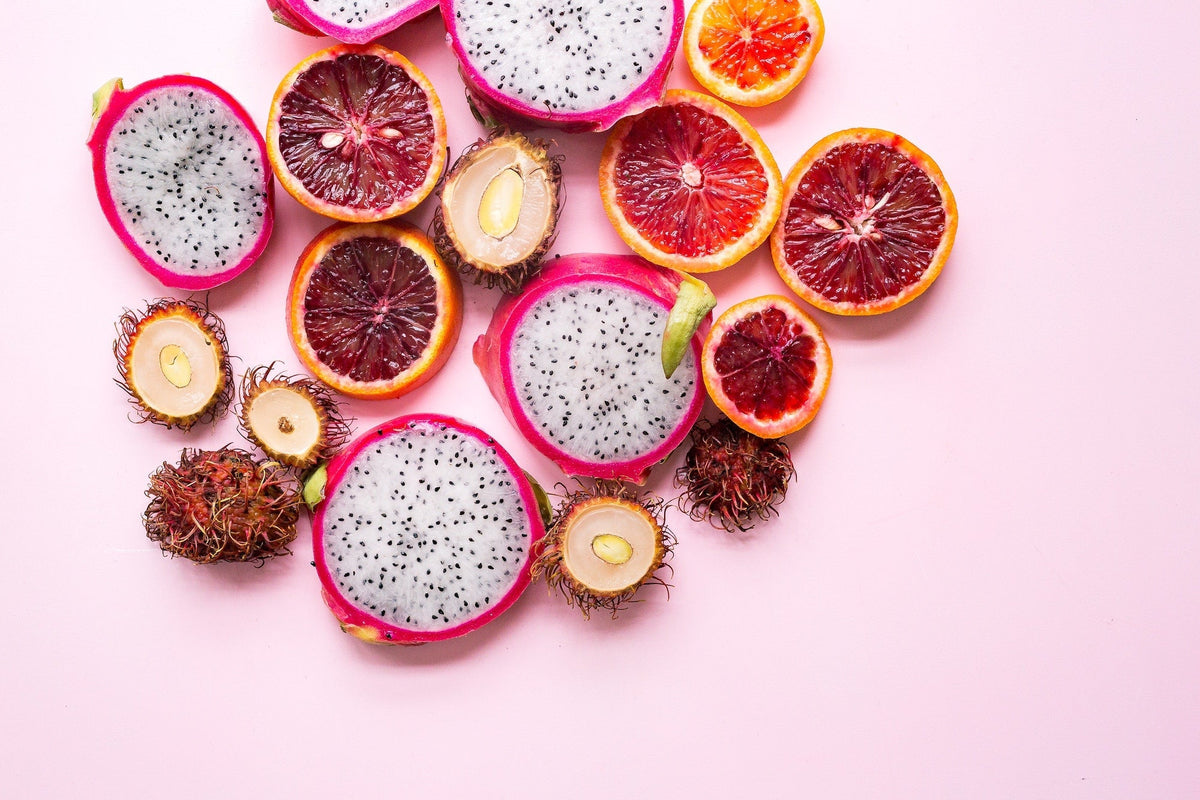 Sliced citrus fruits and dragon fruit arranged on a pink background