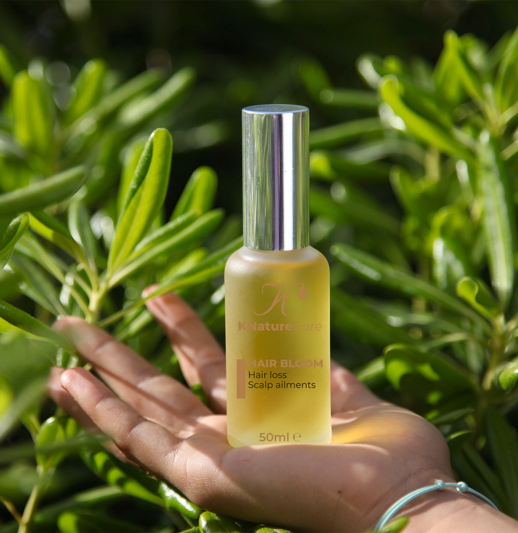 Hand holding the Hair Bloom Scalp Oil bottle among rosemary leaves